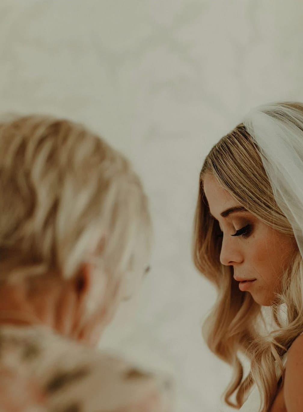 Bride with long, loose blonde waves beneath a veil, eyes lowered