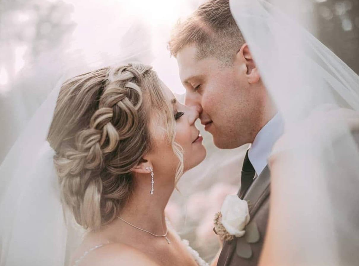Bride with a braided blonde updo, nose to nose with the groom beneath her veil