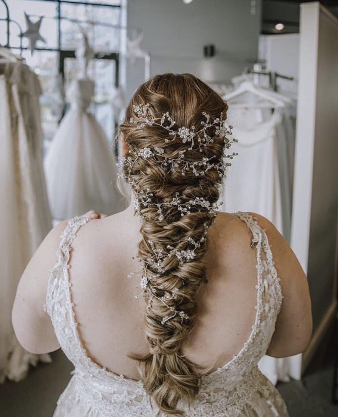 Back view of a long textured braid woven with a floral hair vine, above a lace gown