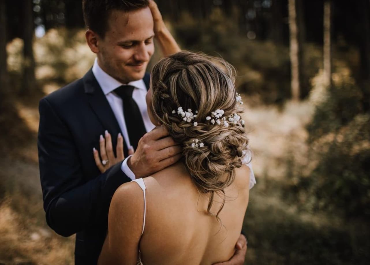 Groom cradling the bride's head, her braided low updo dressed with baby's breath