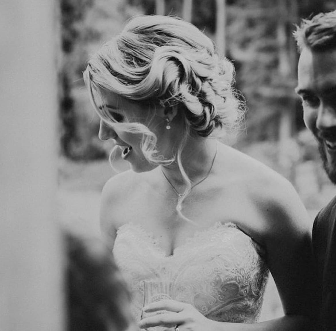 Black-and-white photo of a laughing bride with a softly curled blonde updo