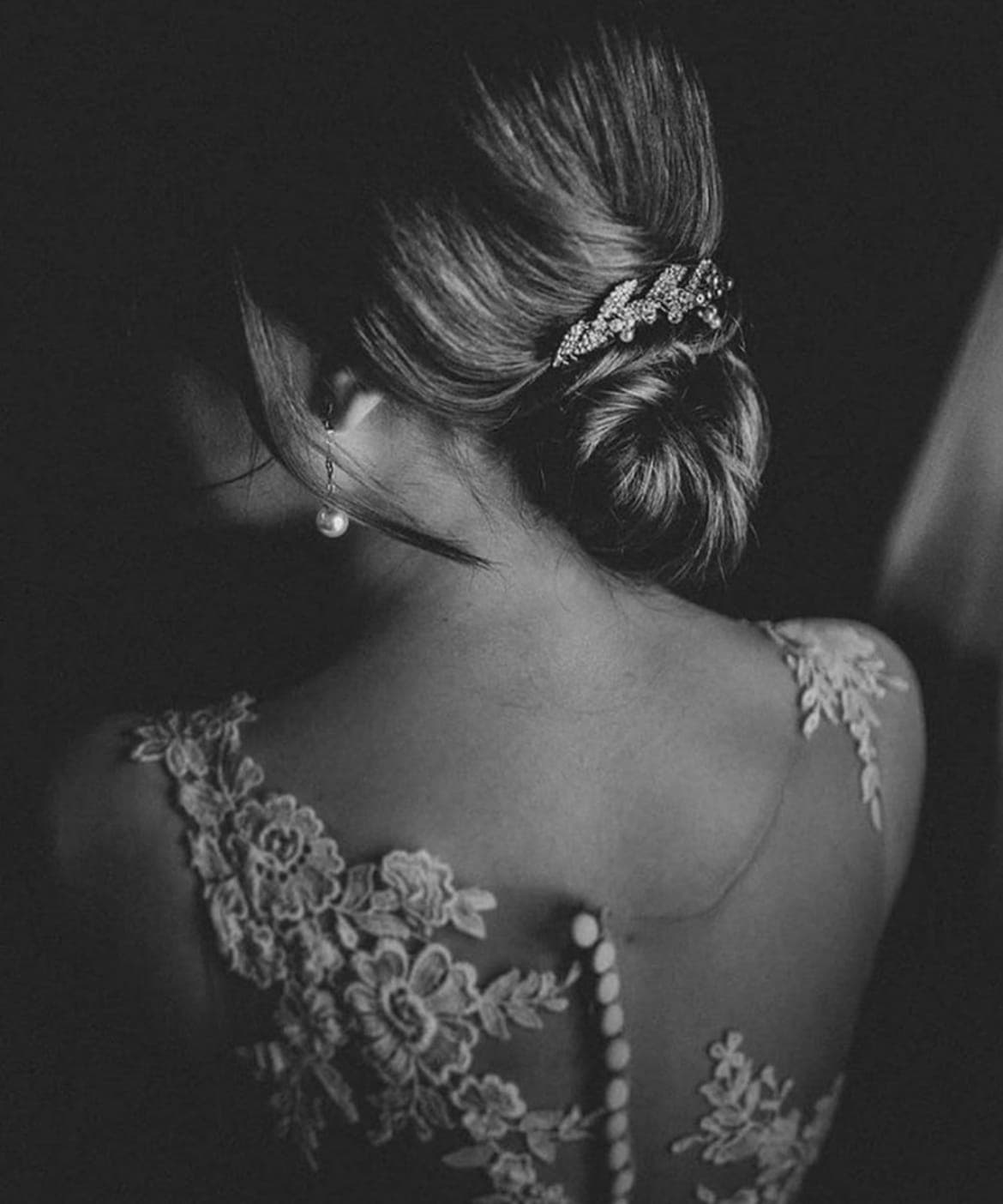 Black-and-white back view of a low bun with a jewelled leaf comb, above a lace gown