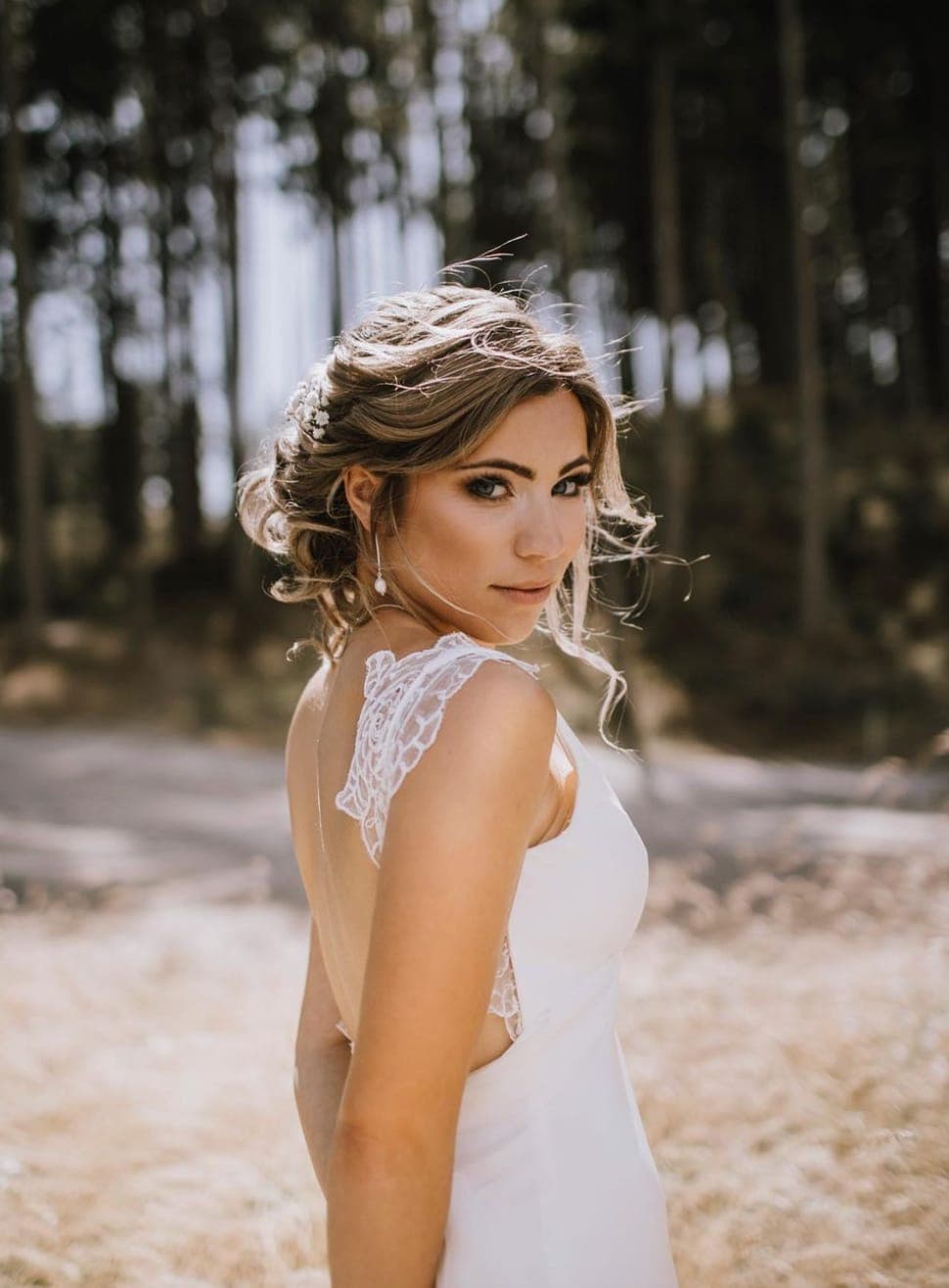 Bride glancing over her shoulder, her loose low updo pinned with small white flowers