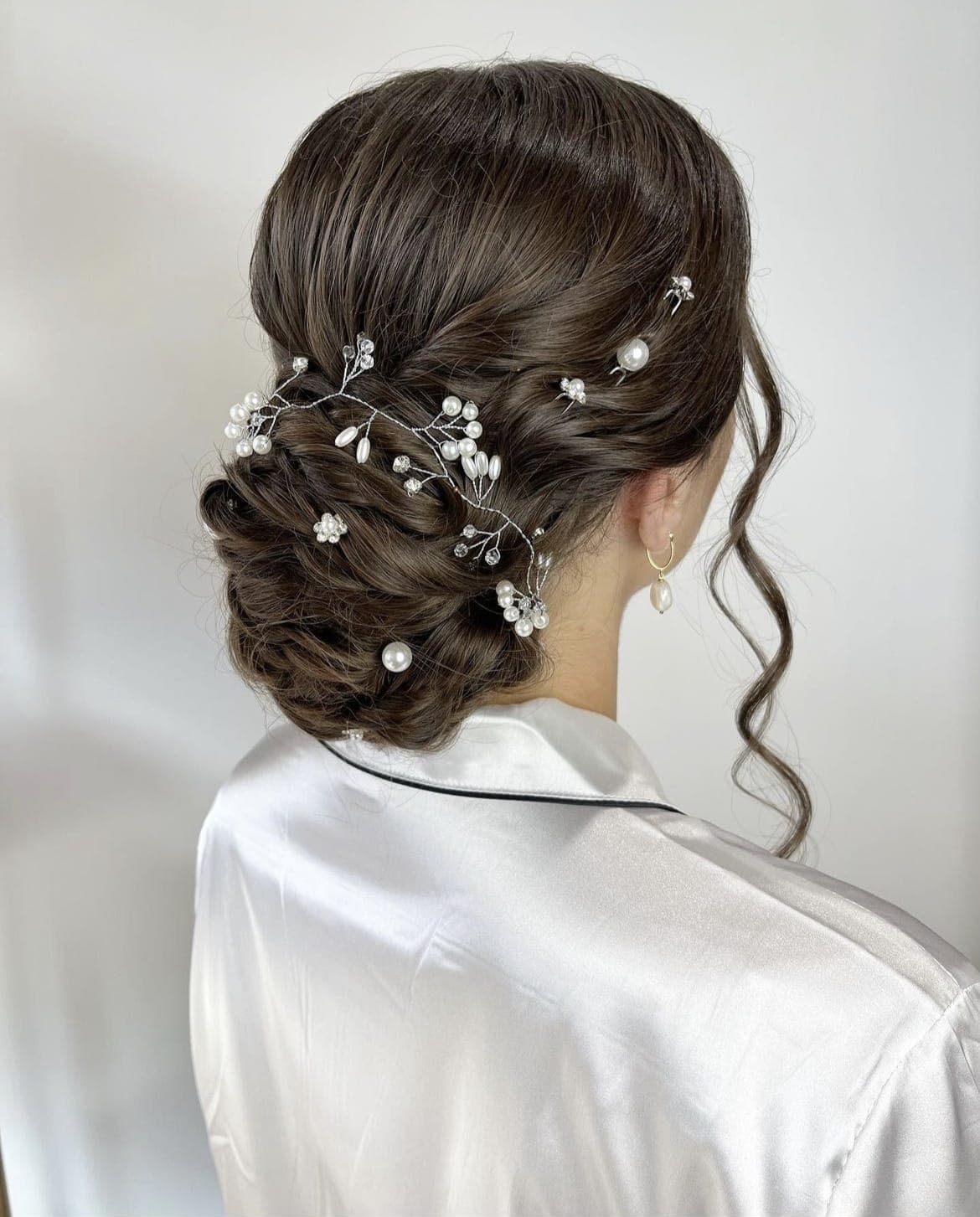 Back view of a dark low updo with loose curls, dressed with a pearl hair vine