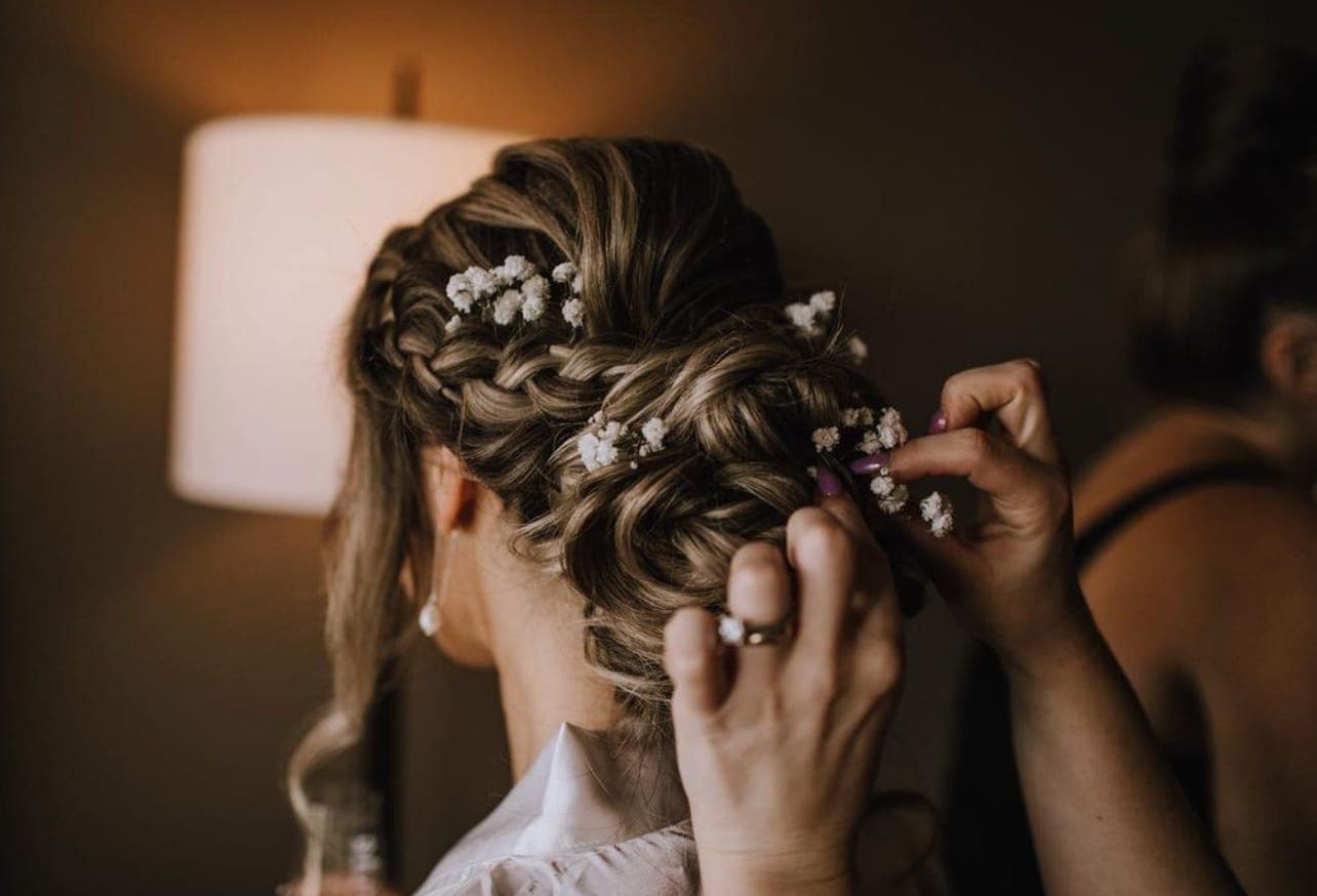Hands placing sprigs of baby's breath into a braided updo