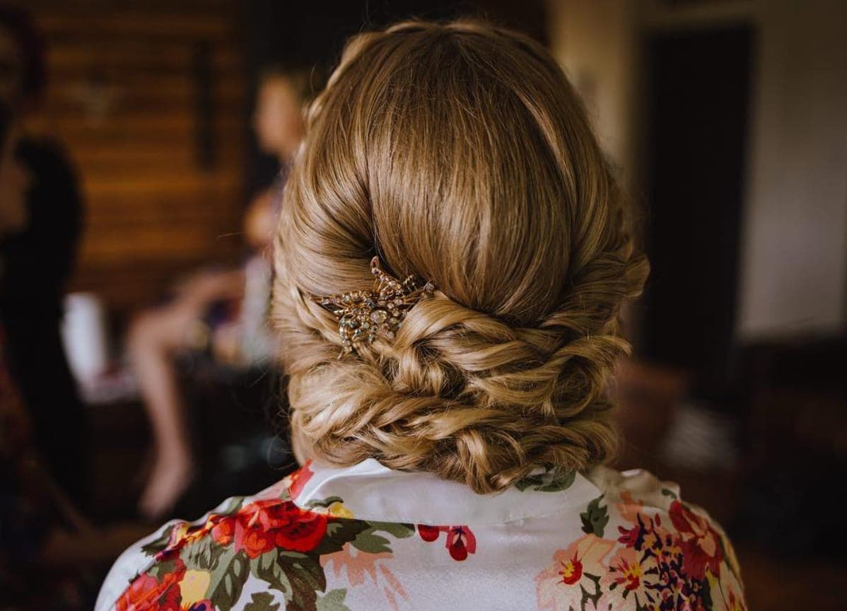 Back view of a twisted honey-blonde low updo with a gold comb, above a floral robe