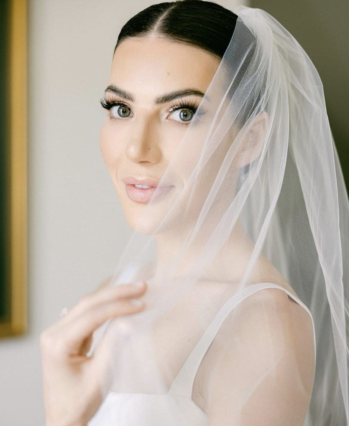 Close portrait of a bride with a sleek centre parting beneath a sheer veil